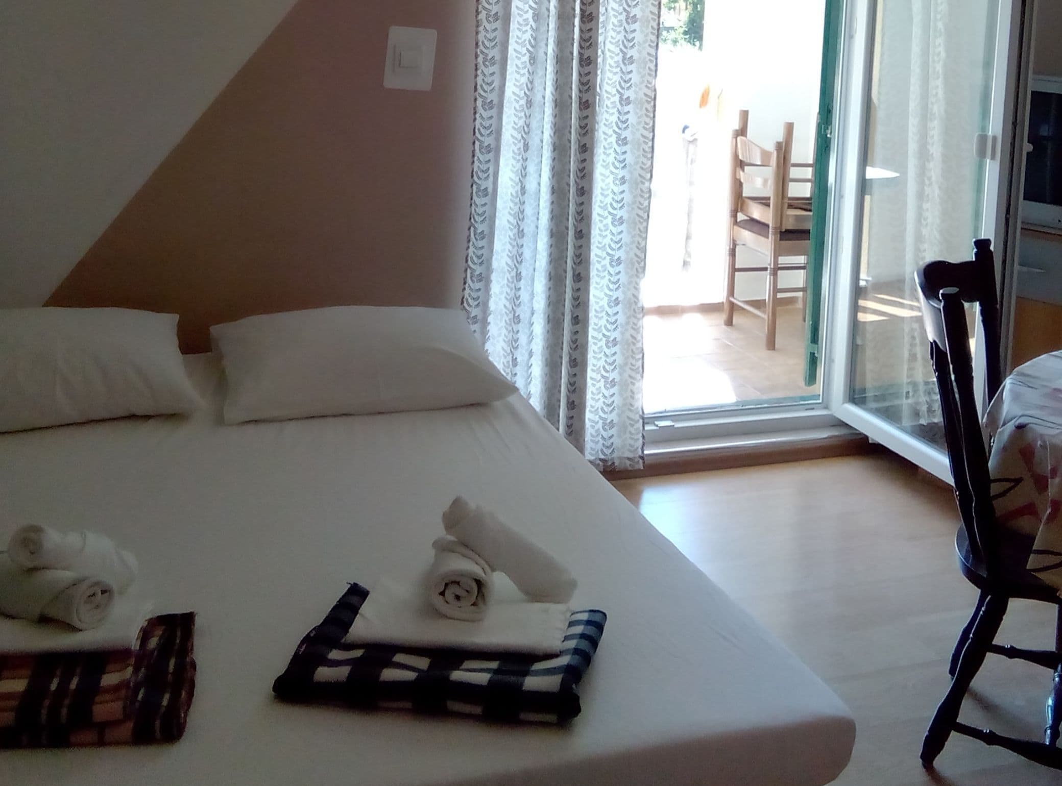 A hotel room with a bed, pillows, a chair, and a window with curtains.