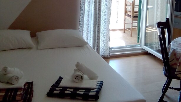 A hotel room with a bed, pillows, a chair, and a window with curtains. - Apartmani Meri (Vodice)