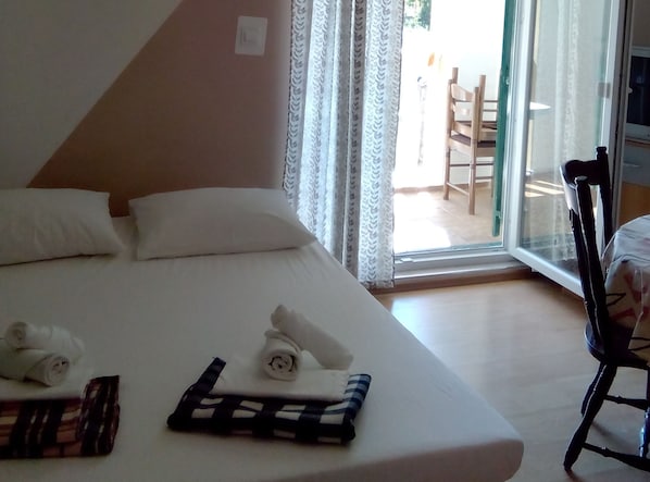 A hotel room with a bed, pillows, a chair, and a window with curtains.