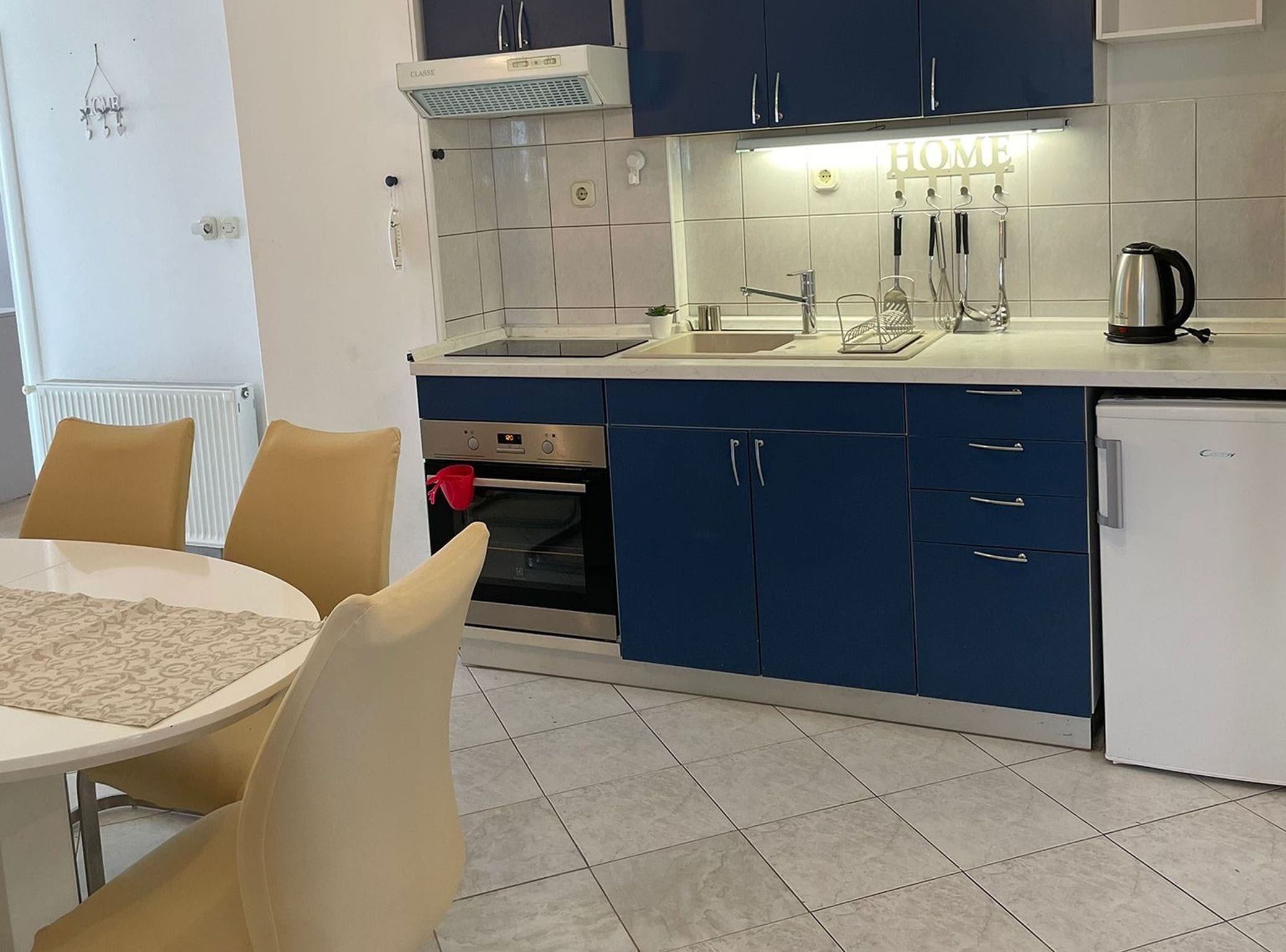 A modern kitchen with blue cabinets, a white refrigerator, and a dining area with a table and chairs.