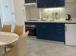 A modern kitchen with blue cabinets, a white refrigerator, and a dining area with a table and chairs.