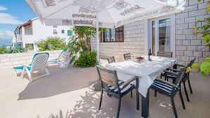 Une terrasse extérieure avec une table dressée pour le repas, entourée de chaises et d’un parasol.