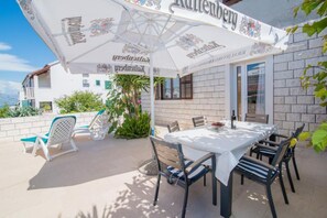 An outdoor patio with a table set for dining, surrounded by chairs and an umbrella. - Apartments Veve - One Bedroom Apartment With Terrace Sea View (Postira)