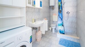 Une salle de bain moderne équipée d’un lave-linge intégré, d’un lavabo, de toilettes et d’un espace douche.