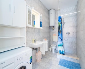 A modern bathroom with a built-in washing machine, a sink, toilet, and a shower area. - Apartments Veve - One Bedroom Apartment With Terrace Sea View (Postira)