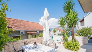 Une terrasse extérieure avec une table et des chaises, un parasol blanc et une vue sur un bâtiment doté d’un toit recouvert de tuiles.