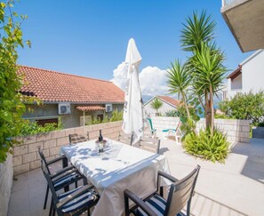 An outdoor patio with a table and chairs, a white umbrella, and a view of a building with a tiled roof. - Apartments Veve - One Bedroom Apartment With Terrace Sea View (Postira)
