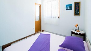 Une pièce avec un lit, une petite table avec une lampe, une porte et une fenêtre avec des rideaux.