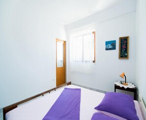 A room with a bed, a small table with a lamp, a door, and a window with curtains. - Apartments Veve - One Bedroom Apartment With Terrace Sea View (Postira)