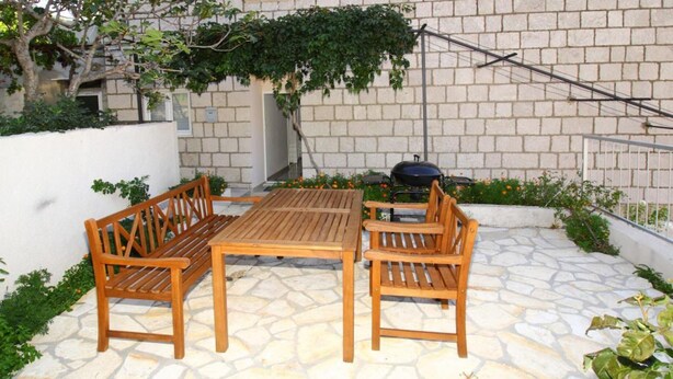 A patio with a wooden table and benches, a barbecue grill, and a stone floor. - Apartment Dubreta With Balcony (Konavle)