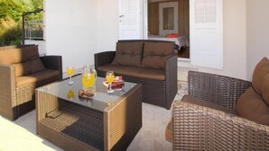 A patio area with wicker furniture, a glass table, and a door leading to an interior room. - Apartment Dubreta With Balcony (Konavle)