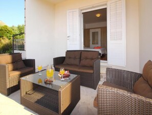 A patio area with wicker furniture, a glass table, and a door leading to an interior room. - Apartment Dubreta With Balcony (Konavle)