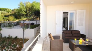 A balcony with wicker furniture, a glass table, and two drinks. - Apartment Dubreta With Balcony (Konavle)