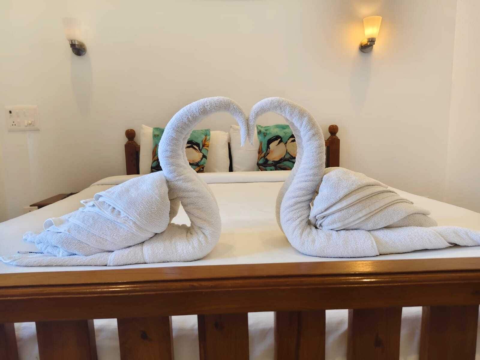 A bed with a wooden headboard, white linens, and two towels arranged in the shape of swans.