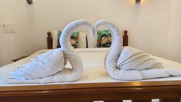 Una cama con cabecera de madera, ropa blanca y dos toallas dispuestas en forma de cisnes.