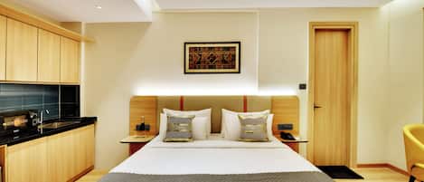 A hotel room with a bed, bedside tables, a desk, a chair, a wardrobe, and a door.