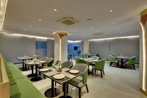 Un comedor moderno con varias mesas y sillas, un pilar central e iluminación empotrada.