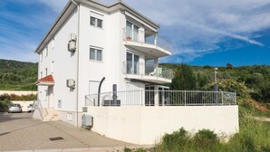 Ein zweistöckiges Wohngebäude mit einem Balkon im oberen Stockwerk, einer gepflasterten Auffahrt und einem umzäunten Grundstück.