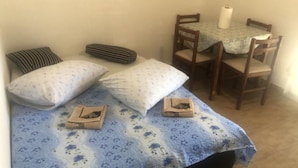 A small room with a bed, two pillows, a striped blanket, a table with a tablecloth, and two chairs. - Apartmani Villa Borzic - One Bedroom Apartment With Terarce (Omis)