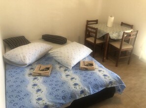 Ein kleines Zimmer mit einem Bett, zwei Kissen, einer gestreiften Decke, einem Tisch mit Tischdecke und zwei Stühlen.