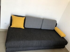 A dark grey sofa with two grey cushions and a yellow pillow against a white wall.