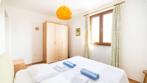 Une chambre d’hôtel avec un lit double, une armoire, une fenêtre avec des rideaux et un luminaire suspendu.