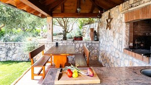 Une terrasse extérieure avec un mur en pierre, une table en bois et une cheminée en briques.
