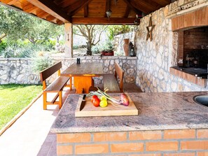 An outdoor patio with a stone wall, a wooden table, and a brick fireplace. - Villa Oliva - Two Bedroom Villa With Terrace and Swimming Pool (Konavle)