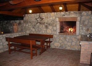 A stone wall with a fireplace, wooden table and benches, and a hanging star decoration. - Villa Oliva - Two Bedroom Villa With Terrace and Swimming Pool (Konavle)