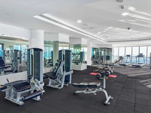 Ein modernes Fitnessstudio mit unterschiedlichen Trainingsgeräten, großen Fenstern und einer hohen Decke.