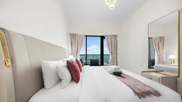 Hotellihuone, jossa on suuri sänky, yöpöytä, peili ja ikkunasta avautuva näkymä kaupungin ylle.