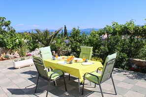 An outdoor dining area with a table set for breakfast, surrounded by chairs, and overlooking a scenic view. - Apartments Gusti - One Bedroom Apartment With Terrace and Sea View (Janjina)