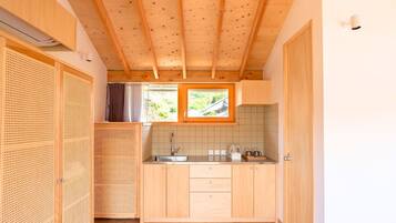 Eine kleine Küche mit Holzausstattung, einer gefliesten Spritzschutzwand und einem Fenster mit Blick auf Grünflächen.