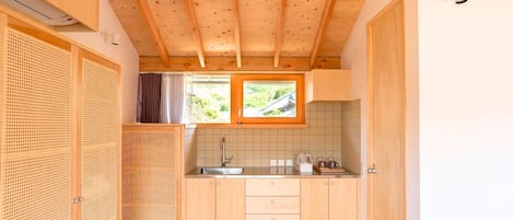 A compact kitchen with wooden cabinets, a tiled backsplash, and a window with a view of greenery.