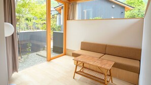Una habitación con techo de madera, un sofá color beige, una mesita tejida y un ventanal corredizo que da a un espacio exterior.