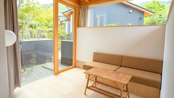Ein Zimmer mit Holzbalkendecke, einem beigefarbenen Sofa, einem gewebten Tisch und einer Schiebetür zu einem Außenbereich.