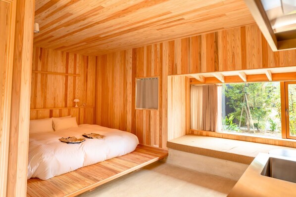 Una habitación de madera con una cama, un rincón con asiento junto a la ventana y un escritorio.