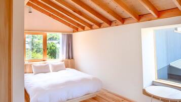 A bedroom with a wooden ceiling, a bed, a window with curtains, and a small table.