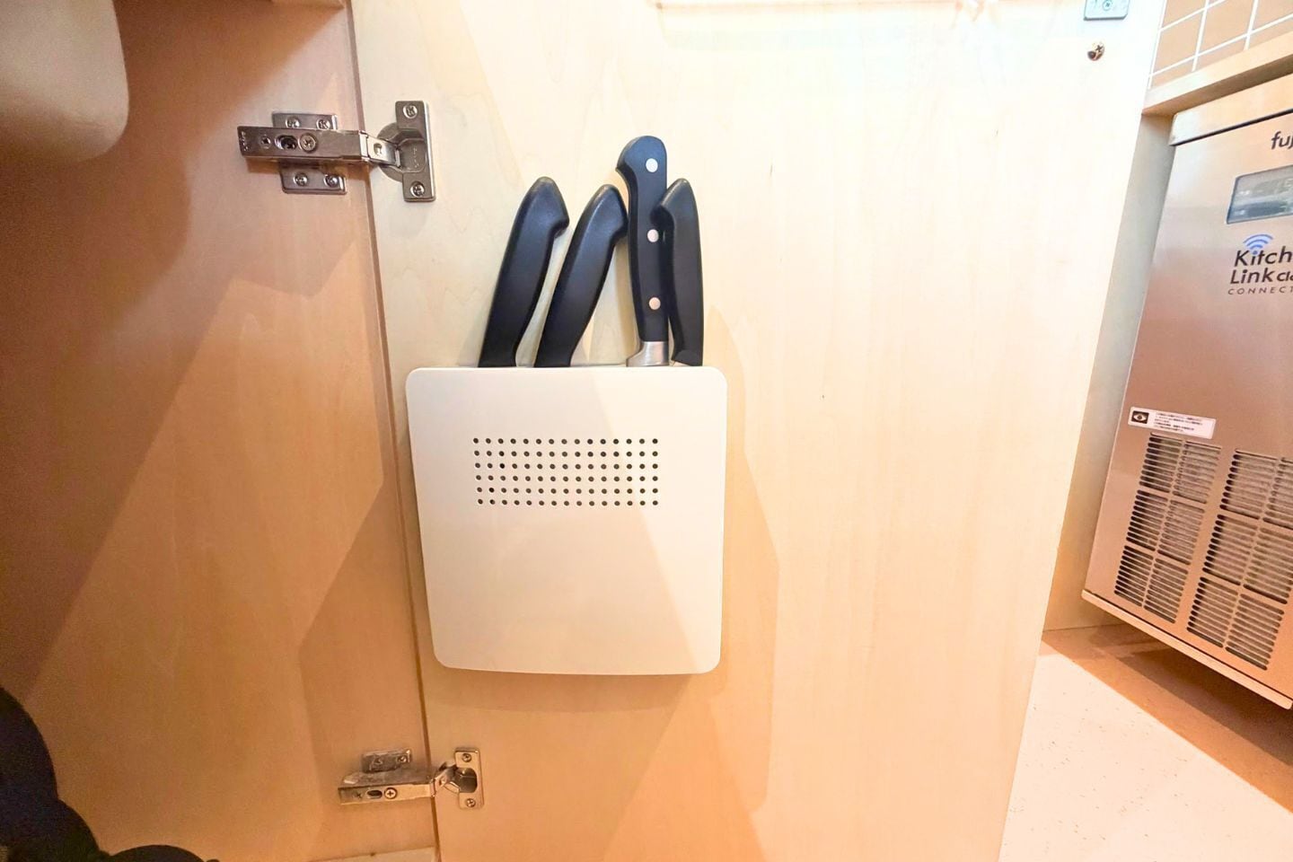 A kitchen with a white wall-mounted knife holder and a kitchen appliance with a label.