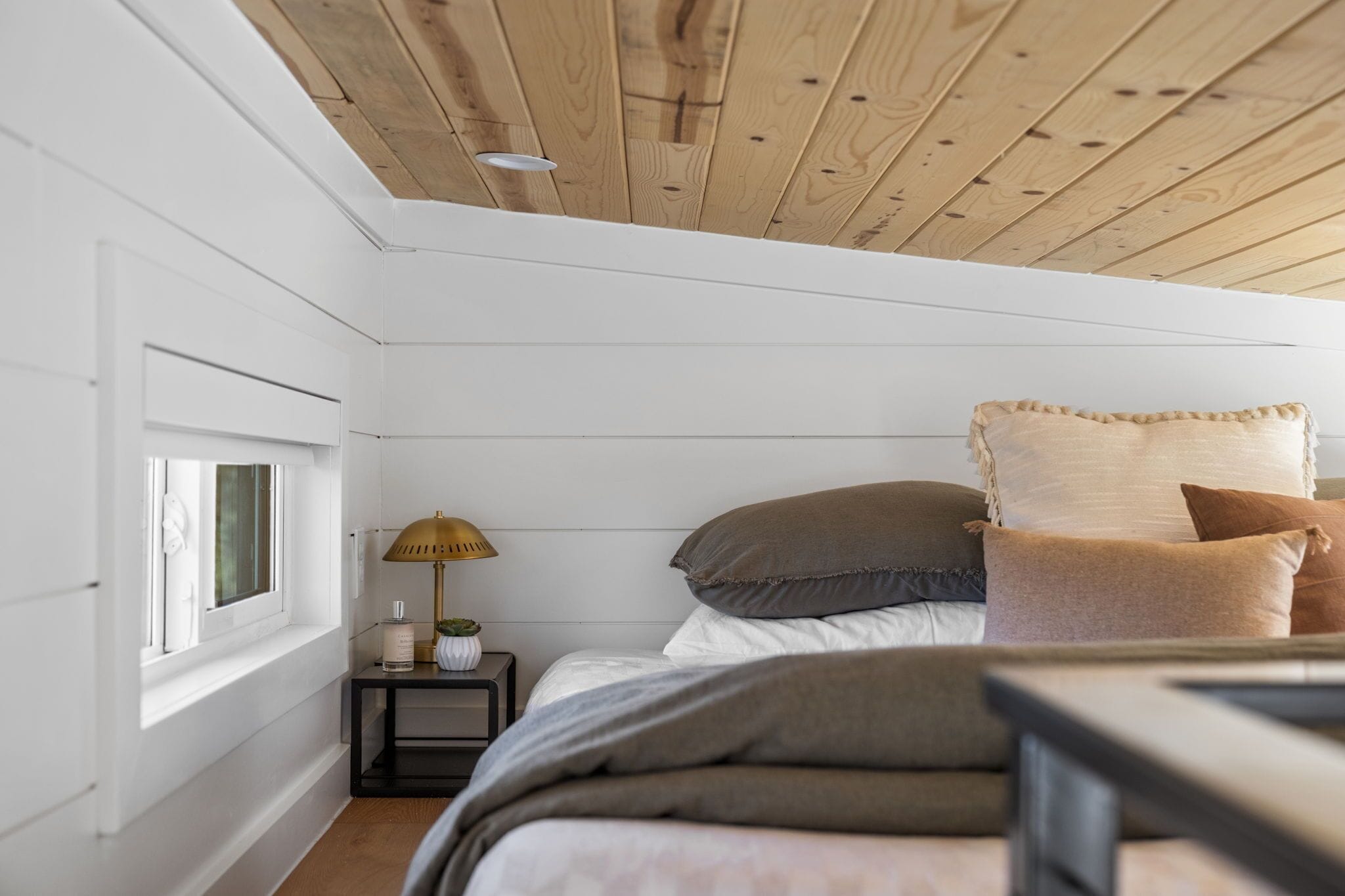 Une chambre avec un plafond en bois, une table de chevet avec une lampe et une fenêtre.