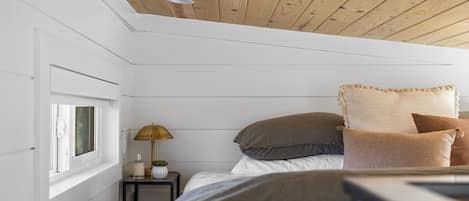 Une chambre avec un plafond en bois, une table de chevet avec une lampe et une fenêtre.