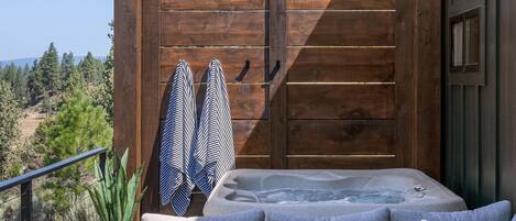 A hot tub with a wooden deck, a railing, and a view of the surrounding landscape.