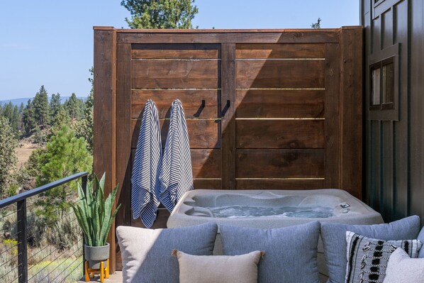 A hot tub with a wooden deck, a railing, and a view of the surrounding landscape.