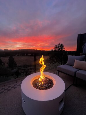 Un espacio de estar al aire libre circular con una chimenea, rodeado por vistas a la puesta de sol sobre el paisaje.