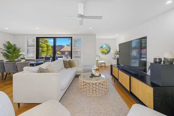 A modern living room with a sofa, coffee table, TV, and a balcony with outdoor furniture.
