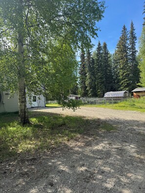 A gravel driveway leading to a fenced area with a house and a shed in the background.