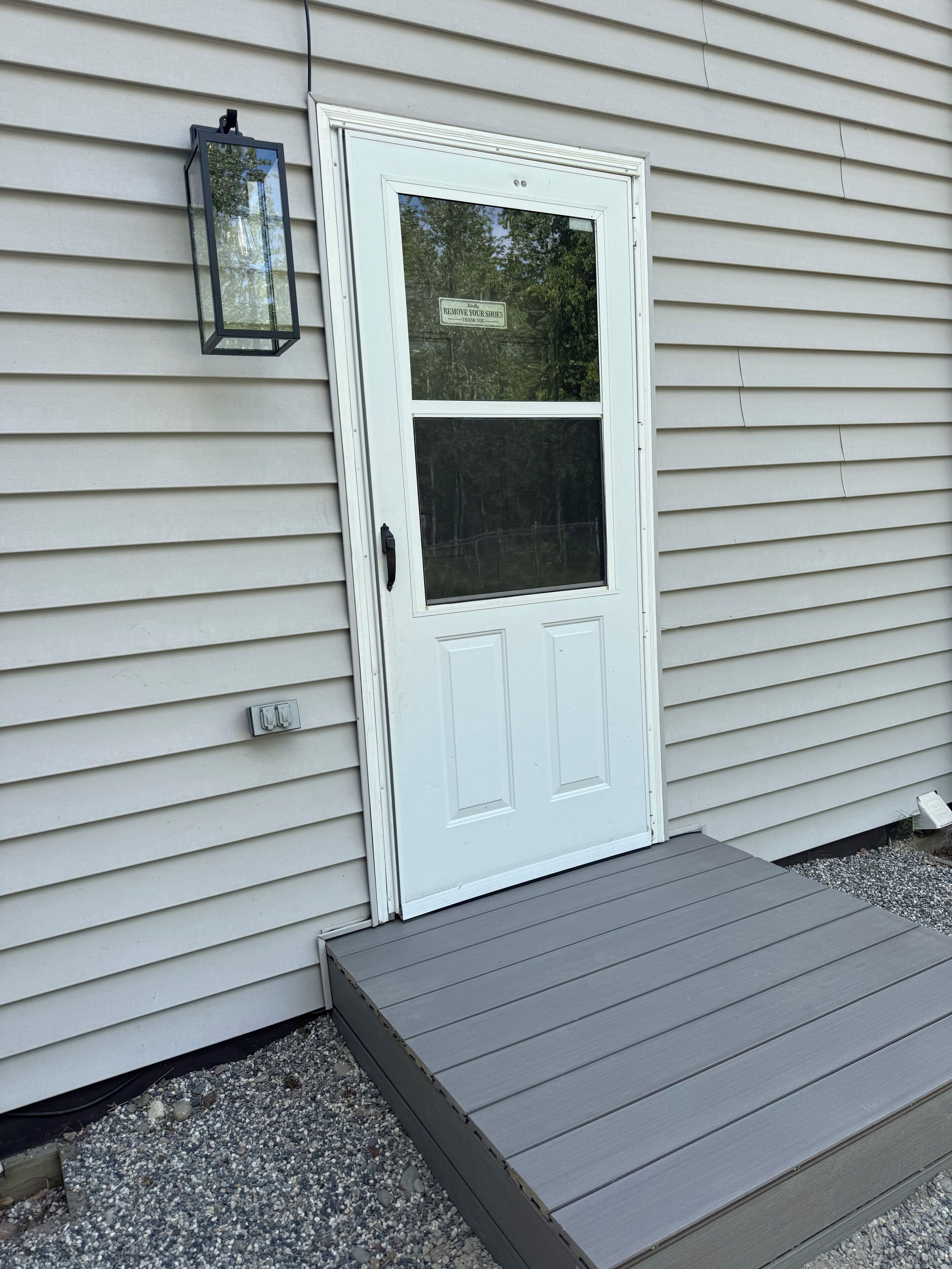 A white door with a window, a small porch, and a wall-mounted light fixture.
