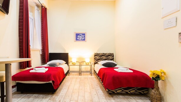 A small hotel room with two beds, a desk, a chair, a lamp, a picture on the wall, and a vase with flowers. - Charming and Historic Old Town Apartments - Twin Room (Zadar)