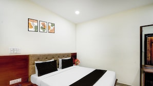 Una cama bien hecha con cabecera, una mesita de noche con lámpara y un enchufe en la pared.