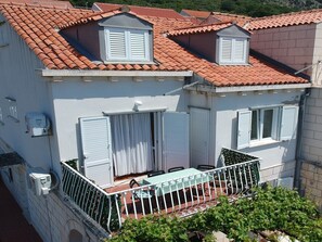 Ein zweistöckiges Gebäude mit rotem Ziegeldach, weißen Fensterläden und einem Balkon mit Tisch und Stühlen.
